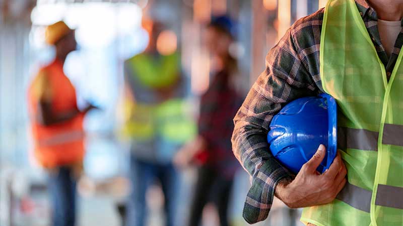 homem com colete refletor e capacete de obras debaixo do braço